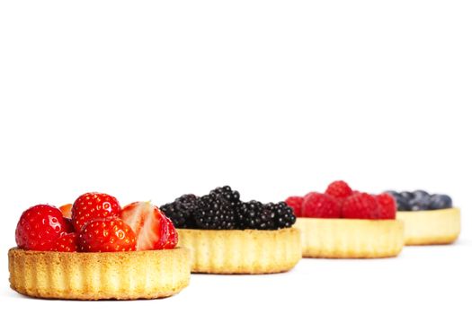 strawberries in a tartlet in front of wild berries in tartlets on white background