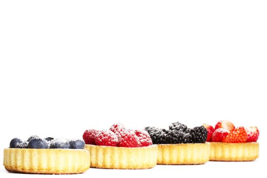 sugar coveres blueberries in front of wild berries in tartlets on white background