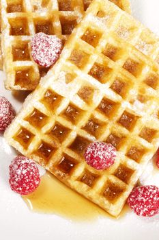 sugar covered raspberries on waffles with syrup from top on white background