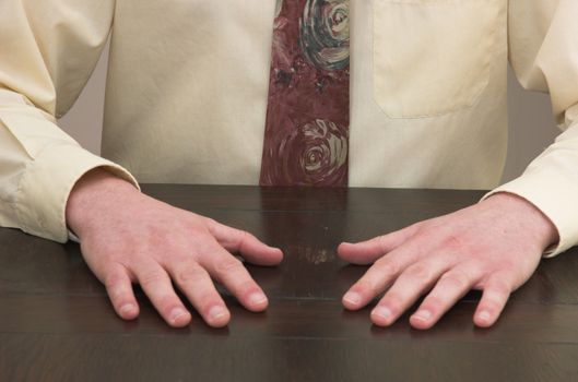 Man sat at desk with hands resting in front of him.