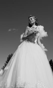 The bride with a bouquet and the sky. The bride in a wedding dress with a bouquet with clouds. Black and white photo.