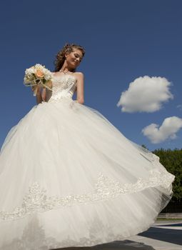 The bride with a bouquet and the sky. The bride in a wedding dress with a bouquet with clouds.