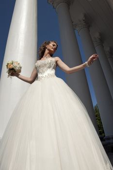 The bride with a bouquet at columns. The bride in a wedding dress with a bouquet near to columns. 