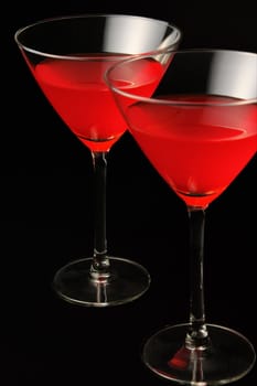 Two cocktail glasses with red drink over black background. Focus on the rear glass.