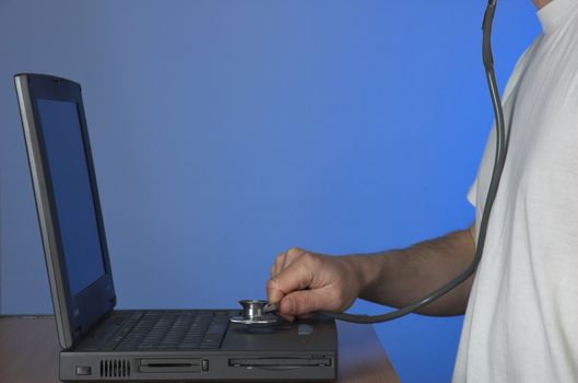 Man working on faulty laptop computer with a doctor's stethoscope. Computer maintenance concept.