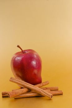 A red delicious apple with cinnamon sticks over a gold background