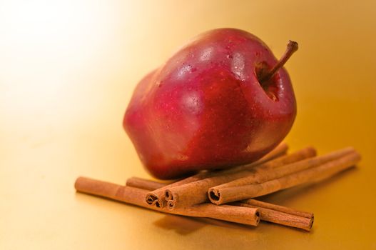 A red delicious apple with cinnamon sticks over a gold background