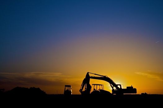 Various pieces of construction equipment are sihouetted by the sunset