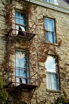A rust colored fire escape over windows with billowing curtains, in a style resembling an oil painting.