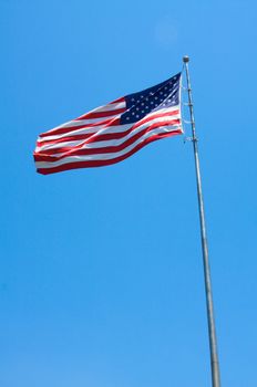 An American flag blows in the wind in front of a blue sky