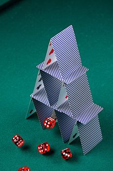 Dice roll perilously close to a house of cards on green felt