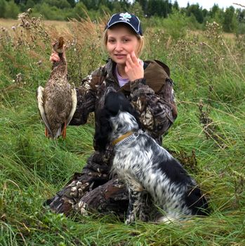 Girl with duck and hunting dog sitting in a field of grass