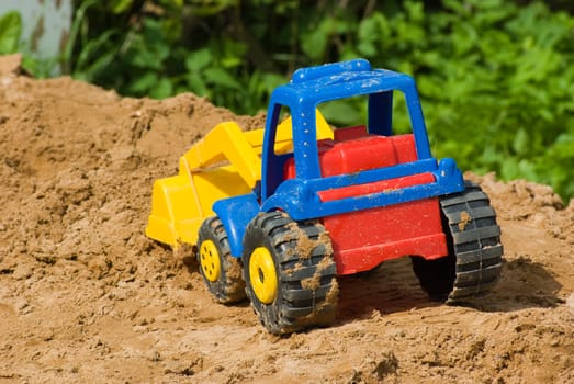 Children's multi-coloured plastic tractor on sand