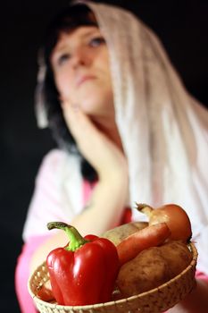 We see young woman who prays her God. In her hands Vegetables