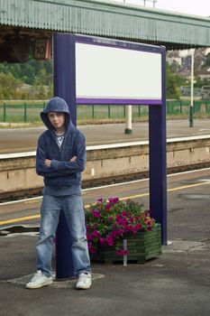 a Hoody or Thug leaning againts a sign post at a train station looking menacing 