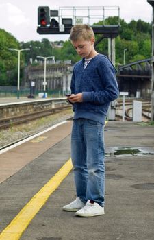 a young teenager using his mobile phone to send a mms or sms message while waiting on a train station platform