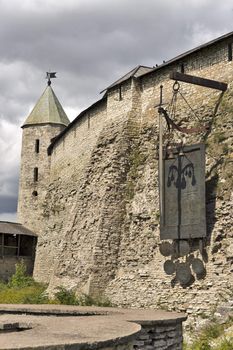 Harsh wall of ancient Pskov kremlin in Russia with monument of shield and sword