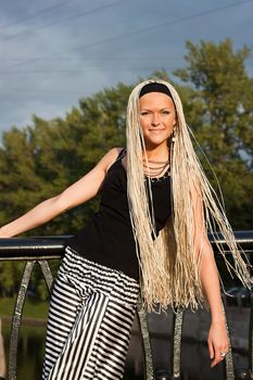 Young woman with braided locks standing on the bridge and smiling