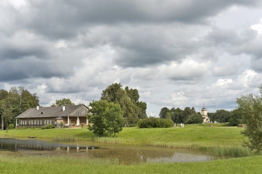 Old farm house, pond and church in cloudy summer day