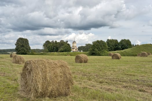 Field with haystacks and a church in cloudy summer day
