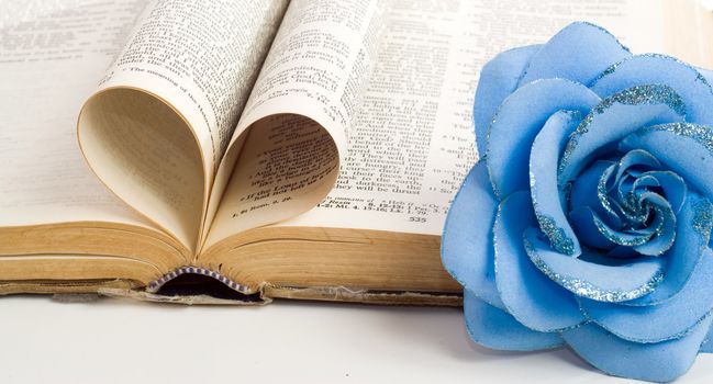 A couple of bible pages folded to make a heart with a artificial flower on the side