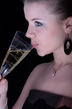 Beautiful blonde drinking a champagne from glass on black background.