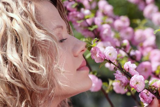 Beautiful blond woman between tree with pink flowers - portrait