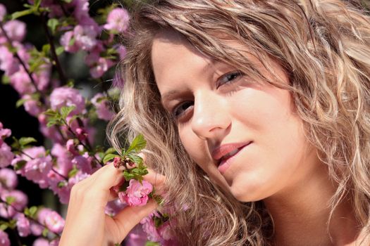 Beautiful blond woman between tree with pink flowers - portrait