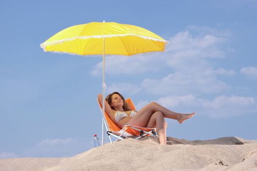 Blond woman in bikini relaxing (sunbathing) under an umbrella on the beach