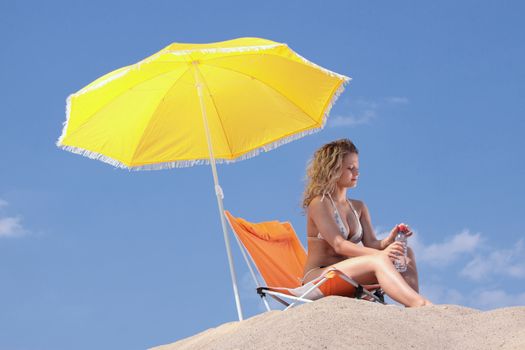 Beautiful blond woman in bikini with bottle of water on beach