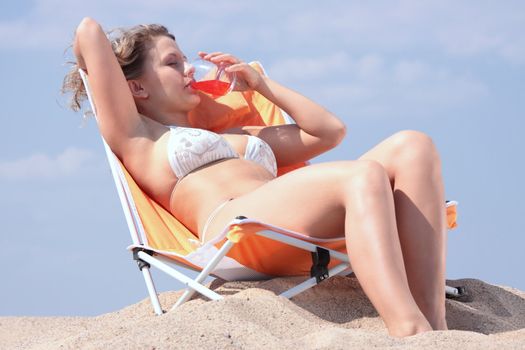 Beautiful blond girl in bikini drinking alcohol cocktail on beach