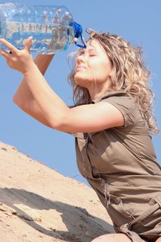 Thirsty blond woman on desert drink from big bottle of water.