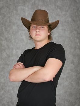 Beautiful serious young man in a cowboy hat on a grey background