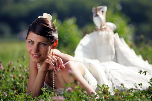 Young adult bride lying in summer field or meadow, smiling.