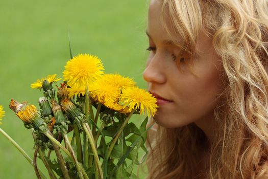 Beautiful young blond woman (girl) in a field enjoying the sun and smelling the yellow flowers