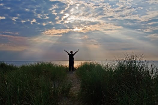 A person is standing on top of dunes greeting the sun