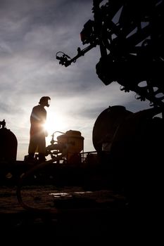 A silhouette of a high clearance sprayer being filled