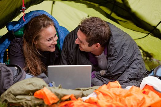 A happy couple in a tent using a computer looking at each other