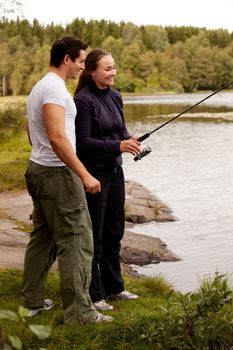 A young adult couple having fun fishing on a forest lake.