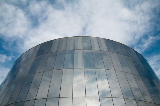 Glass round building with cloudy sky reflecting.