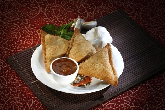 three indian samosas on a white plate with sauce