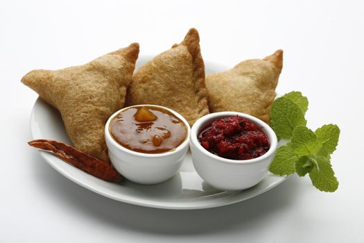 three indian samosas on a white plate with sauce
