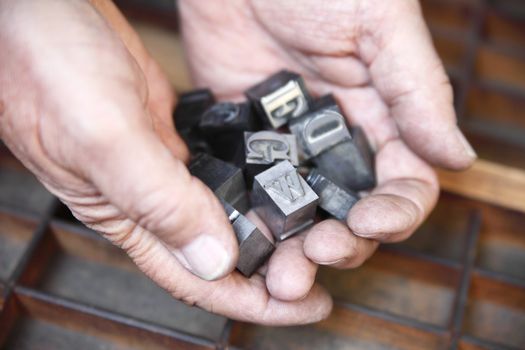 hands holding lead letterpress type over a wood typecase background