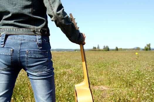 A woman holding a guitar looking at an empty field