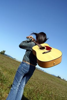 A woman holding a guitar looking at an empty field