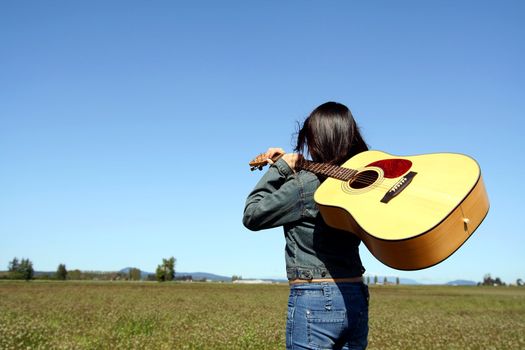 A woman holding a guitar looking at an empty field