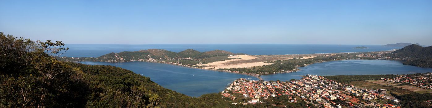 A panoramic image of a far view of a city lake with the ocean as a background. This is Lagoa da Conceição in Florianópolis, Brazil. 