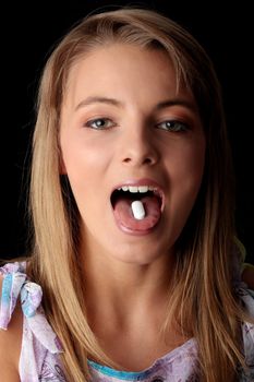 Young woman eating a pill isolated on black background