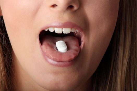 Young woman eating a pill isolated on black background