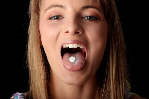 Young woman eating a pill isolated on black background